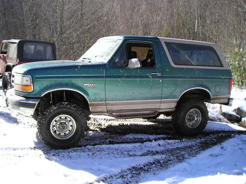 1996 Ford Bronco - A green Ford Bronco with tan trim is seen in a snowy, off-road environment next to another vehicle.