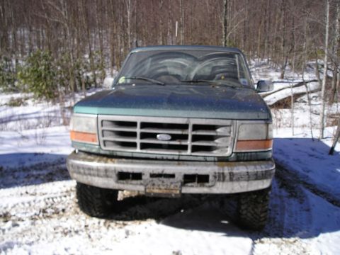 1996 Ford Bronco - A green 1996 Ford Bronco is parked in a snowy, wooded area, facing the camera.