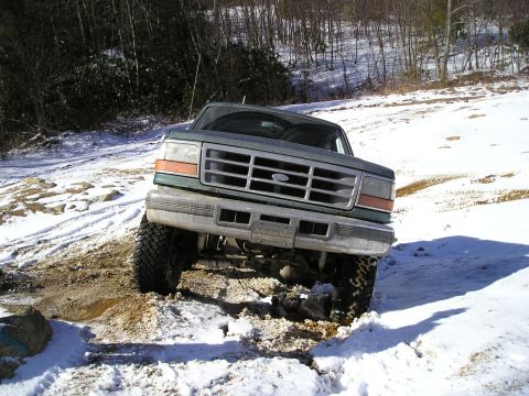 1996 Ford Bronco - A Ford F-Series truck navigates a snowy and muddy terrain, with trees in the background.