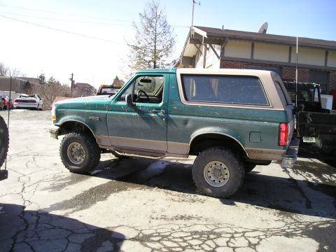 1996 Ford Bronco - A green 1996 Ford Bronco with a tan removable top is parked on a cracked asphalt surface.