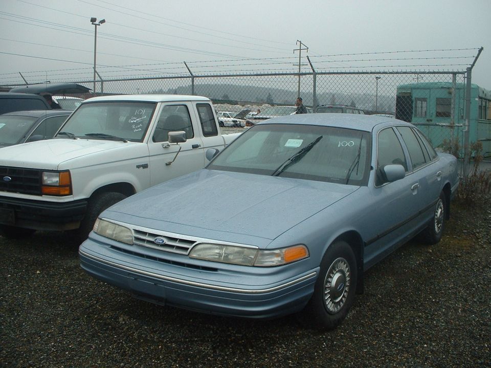 Light blue 1999 Ford Crown Victoria, 3/4 front view. White truck in background