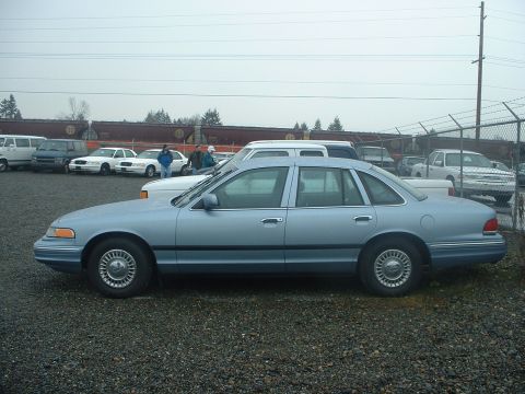 1999 Ford Crown Victoria - This light blue 1999 Ford Crown Victoria is seen from the side in a lot with other vehicles.