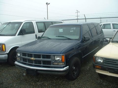 1999 Ford Crown Victoria - A dark blue SUV is parked next to a white van and a beige car. The SUV has a prominent chrome grille and appears to be from the mid-1990s.