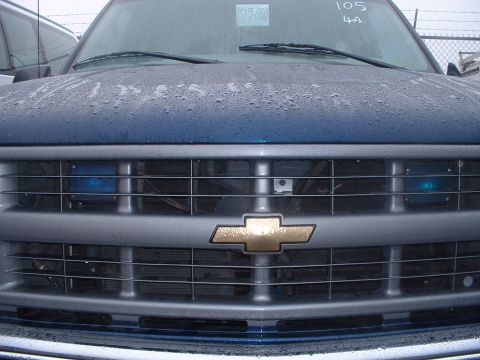 1999 Ford Crown Victoria - Close-up of a blue Chevrolet C/K pickup truck's front grille and hood, showing water droplets.