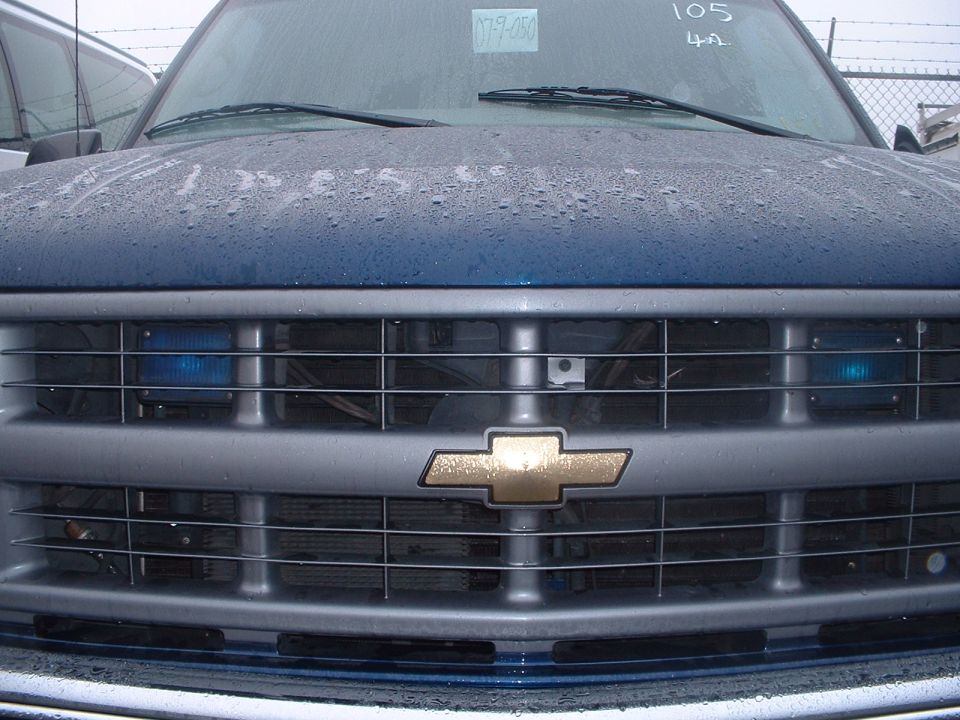 Front grille and hood of a blue Chevrolet C/K pickup truck, possibly 1995 model year. Water droplets on the hood