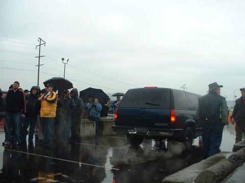 1999 Ford Crown Victoria - A dark blue SUV emits exhaust smoke on a rainy day as onlookers stand under umbrellas.