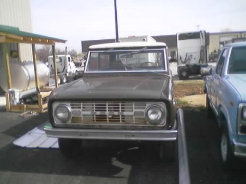 1989 Ford Bronco - A 1973 Ford Bronco is parked next to a blue pickup truck, with semi-trucks in the background.