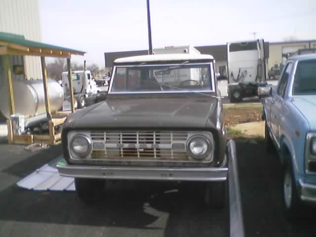 Front view of a 1973 Ford Bronco parked next to a blue pickup truck