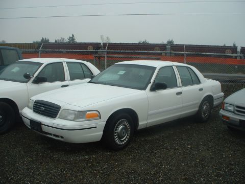 1999 Ford Crown Victoria - Two white sedans are parked in an outdoor lot with a train track in the background.