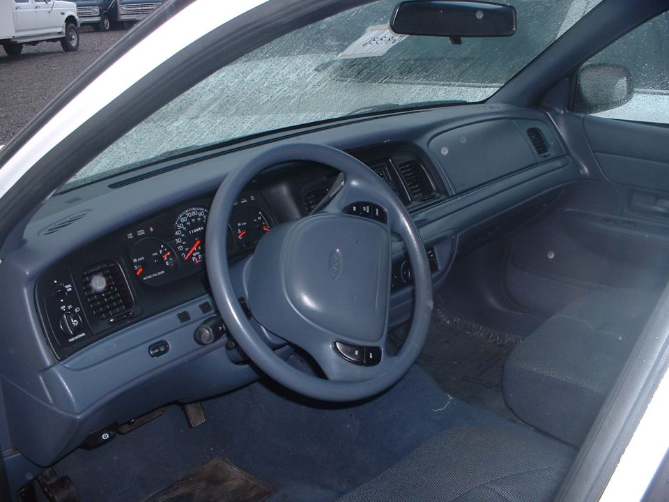 Interior of a white 1998 Ford Crown Victoria showing the dashboard, steering wheel, and driver's seat