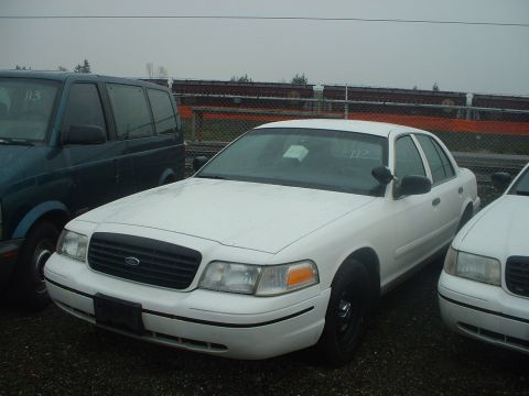 1999 Ford Crown Victoria - A white 1998 Ford Crown Victoria is parked next to another vehicle, with a dark van to its left.