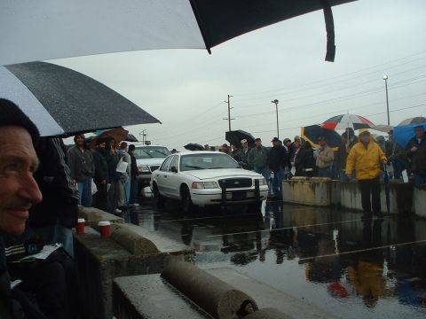 1999 Ford Crown Victoria - A white 1999 Ford Crown Victoria is presented at an outdoor auction on a rainy day, with attendees holding umbrellas.