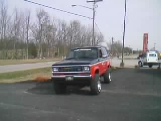 1989 Ford Bronco - Low-resolution front three-quarter shot of a lifted two-tone black-and-red full-size Bronco-style 4x4 SUV parked at the edge of a lot, with…