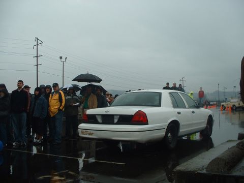 1999 Ford Crown Victoria - A white 1999 Ford Crown Victoria is viewed from the rear at an outdoor auction on a rainy day.