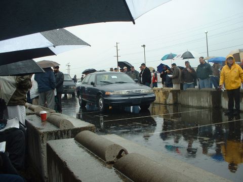 1999 Ford Crown Victoria - A dark blue 1999 Ford Crown Victoria is presented at an outdoor auction event in the rain.