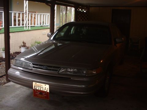 1999 Ford Crown Victoria - A brown Ford Crown Victoria is parked under a carport, showing its front grille and headlights.