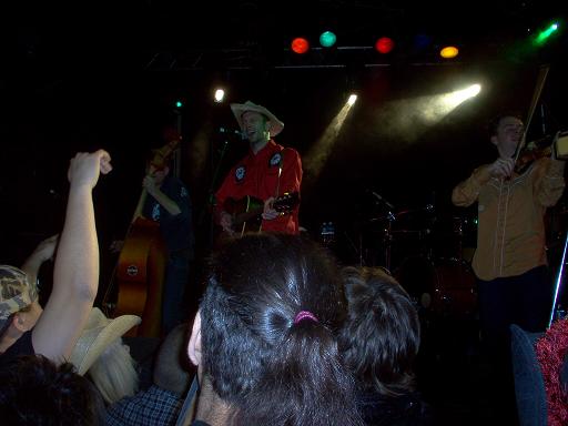 Band performing on a dimly lit stage with spotlights and colorful lights overhead
