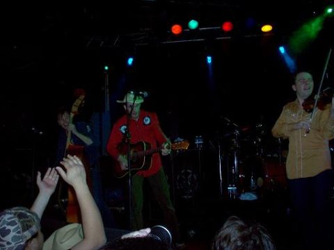 1988 Ford Bronco - A band plays live music on a stage, illuminated by colorful lights, with members playing guitar, bass, and violin.