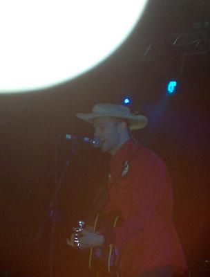 1988 Ford Bronco - A musician performs on stage under a bright spotlight, wearing a cowboy hat and a red jacket.