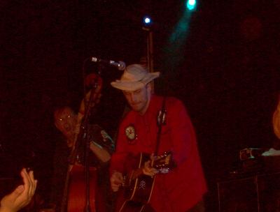 1988 Ford Bronco - A musician performs on stage, wearing a red shirt and a cowboy hat while playing an acoustic guitar.