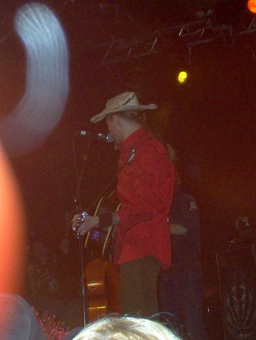 1988 Ford Bronco - A performer in a cowboy hat and red shirt is on stage, holding a guitar.