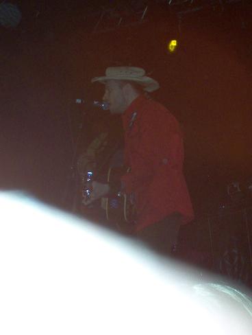1988 Ford Bronco - A musician wearing a cowboy hat and red jacket performs on stage, playing an acoustic guitar.