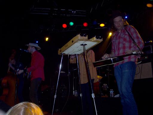 Band playing music on a stage with lights. One guy plays a lap steel guitar