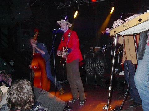 1988 Ford Bronco - A band performs live music on stage, a singer, bassist, and keyboardist.