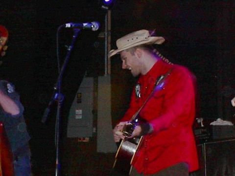 1988 Ford Bronco - A musician performs on stage, wearing a cowboy hat and a red shirt while playing an acoustic guitar.