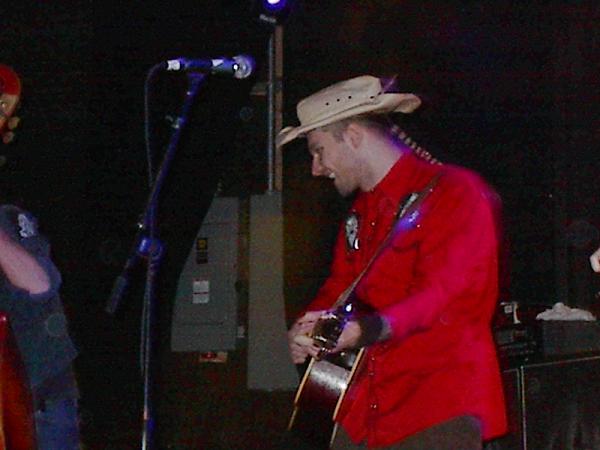 Man in red shirt and cowboy hat plays guitar on stage