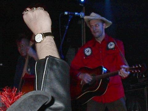 1988 Ford Bronco - A musician performs on stage, wearing a red shirt and a cowboy hat while playing an acoustic guitar.