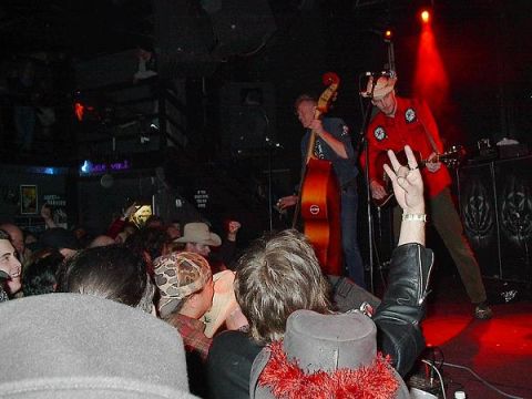 1988 Ford Bronco - A band performs live on stage in a dimly lit venue, with a bassist and guitarist playing to an audience.