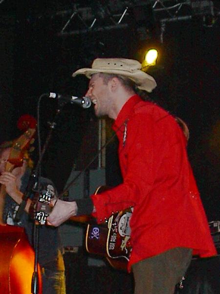 1988 Ford Bronco - A musician wearing a cowboy hat and a red shirt performs on stage, singing into a microphone.
