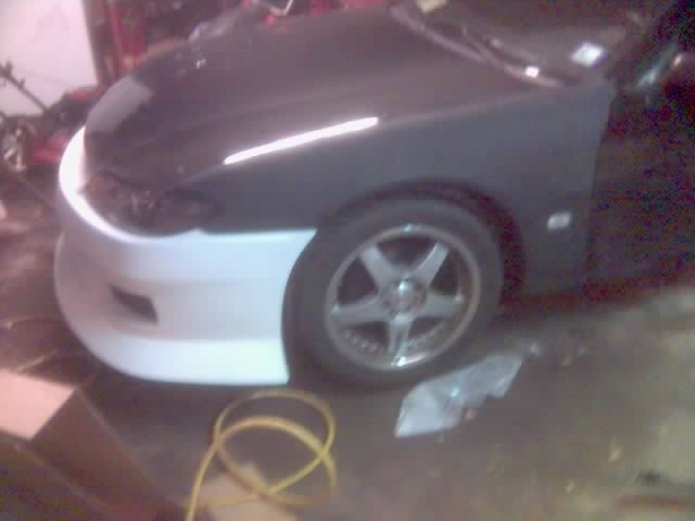 Nissan 240SX in garage with white front bumper on black primered body, chrome five-spoke wheels