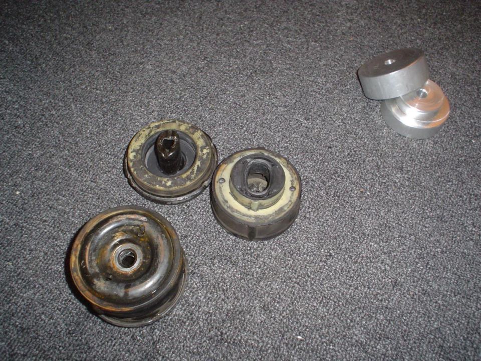 Four used rubber and metal car parts on a gray carpeted surface