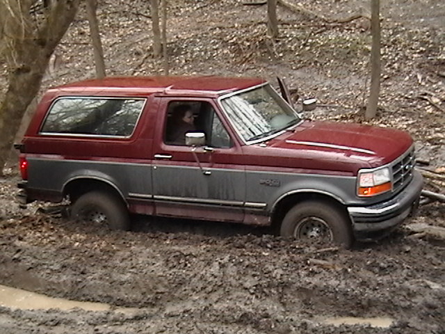 Maroon and gray Ford Bronco stuck in thick mud off-road