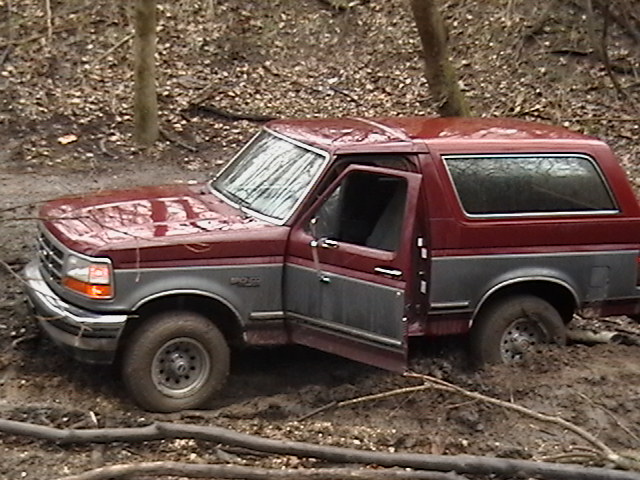 Red and gray Ford Bronco stuck in mud, driver's door open
