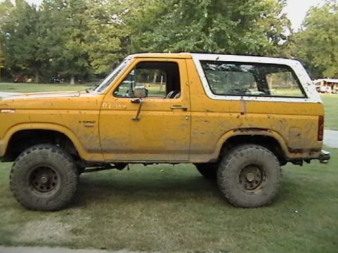 1986 Ford Bronco - This yellow Ford Bronco is shown from the side, covered in mud, with a white removable top.