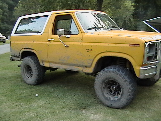 Yellow Ford Bronco with white top, lifted suspension, and off-road tires, covered in mud