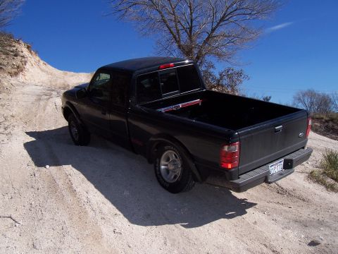 2003 Ford Ranger - A black 2003 Ford Ranger pickup truck navigates a dusty, off-road path under a clear blue sky.