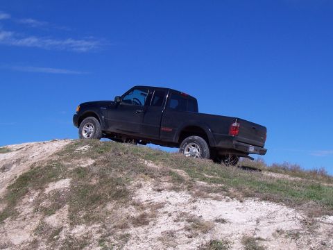 2003 Ford Ranger - A black 2003 Ford Ranger pickup truck navigates an off-road dirt incline against a bright blue sky.