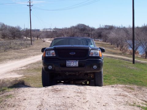 2003 Ford Ranger - Black 2003 Ford Ranger parked on a dirt path with trees and a body of water in the background.