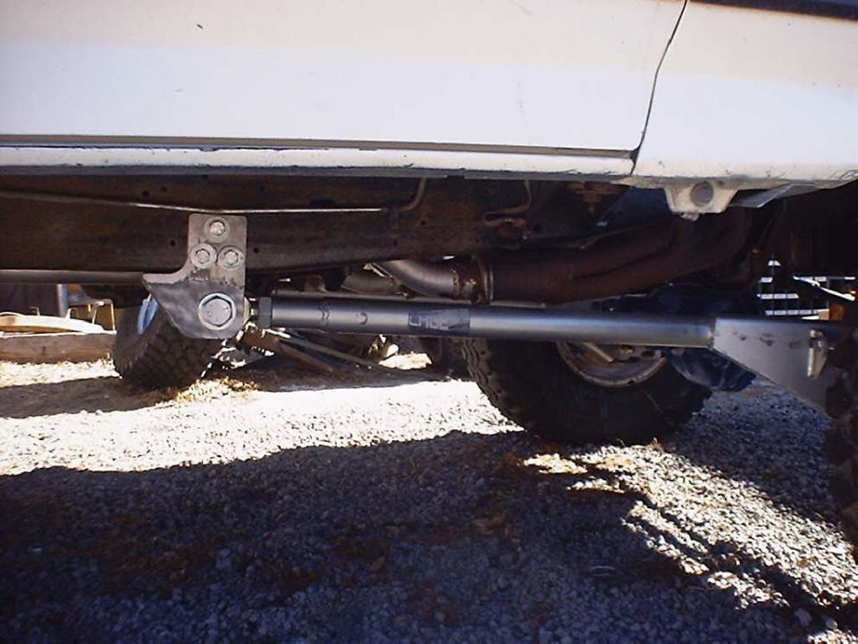 Underside of a white lifted 4x4 showing a fabricated traction bar between axle and frame