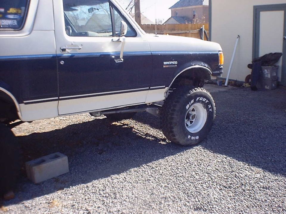 White and dark blue Ford Bronco with lifted suspension and "Bigfoot" tires