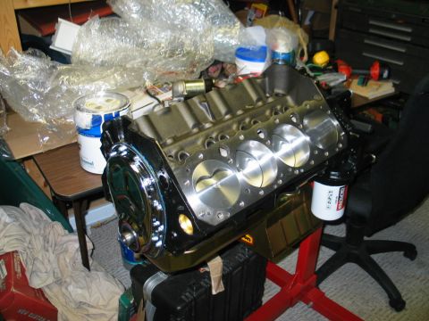 1981 Chevrolet Corvette - Engine block with pistons visible, chrome front cover, on a red stand in a cluttered garage.