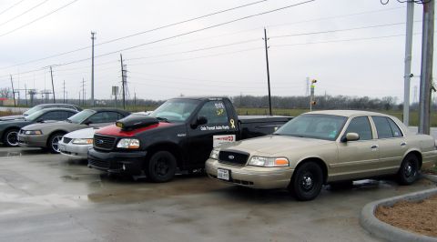 2000 Ford Crown Victoria - A row of vehicles, including a tan 2000 Ford Crown Victoria and a black pickup truck, are parked outdoors on a cloudy day.