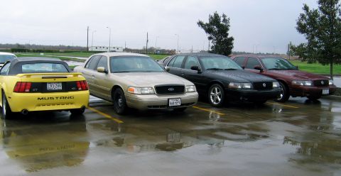2000 Ford Crown Victoria - A gold 2000 Ford Crown Victoria is parked in a lot alongside other vehicles on a wet day.