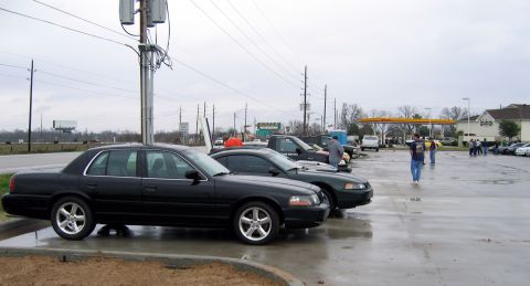 2000 Ford Crown Victoria - Several vehicles are parked in a wet lot under an overcast sky, with a gas station visible in the background.