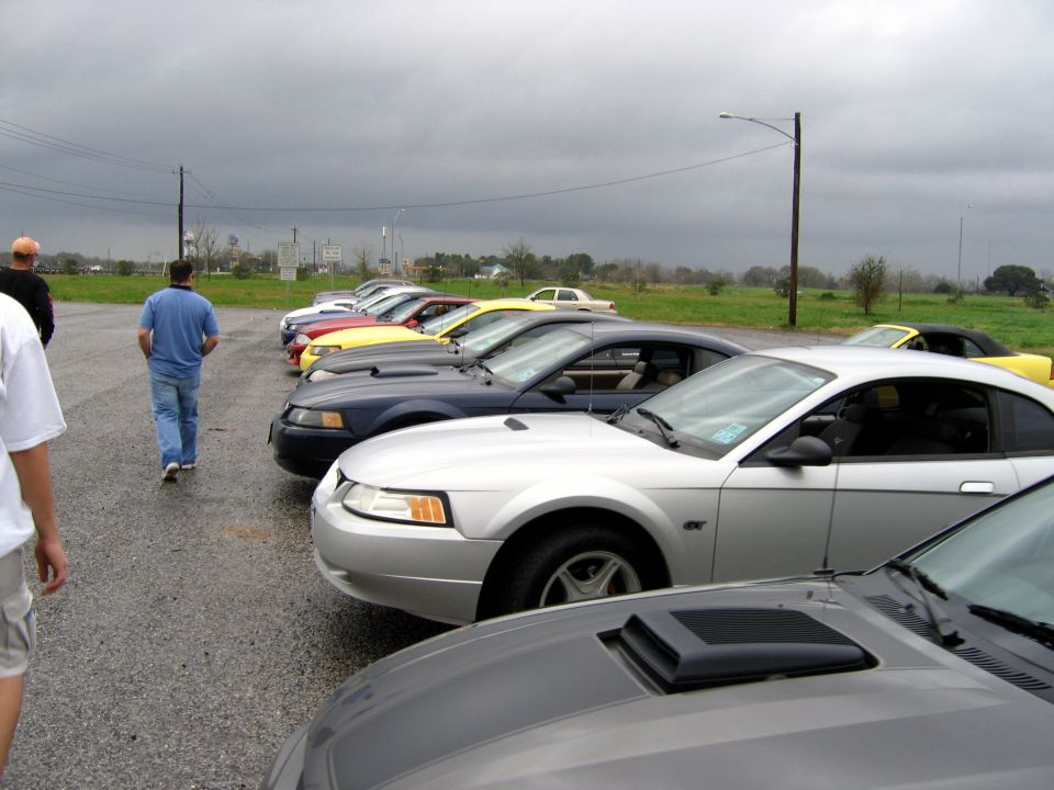 Silver 2000 Ford Mustang coupe parked in a line on a wet asphalt lot under a cloudy sky