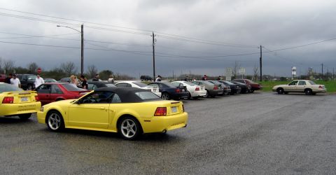 2000 Ford Crown Victoria - A row of cars, including a tan 2000 Ford Crown Victoria, are parked under an overcast sky.